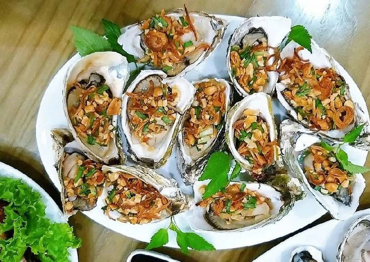 Hàu nướng mỡ hành bày trên đĩa trắng, phủ hành phi và rau thơm