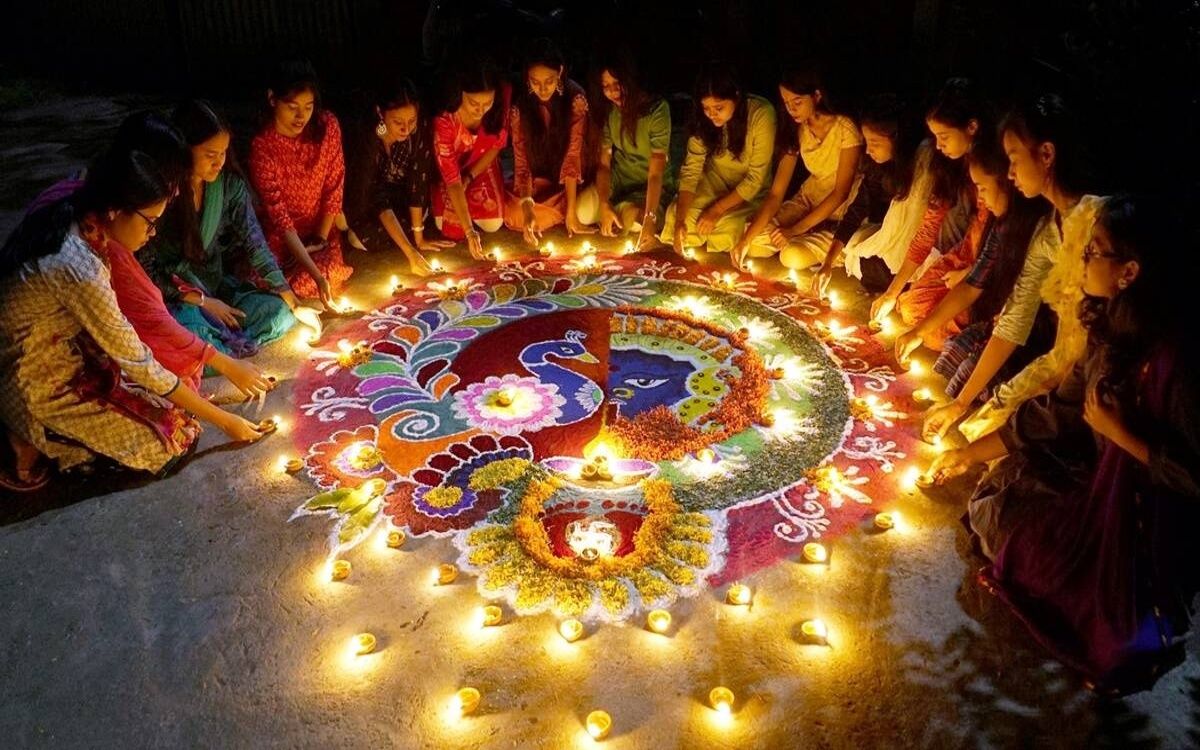 Everyone lights candles around floral and colorful powder rangolis, creating a warm Diwali ambiance.