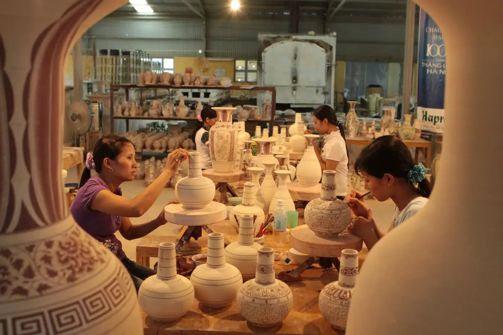 The scene of ceramic artisans sitting around a table, focused on painting patterns on white ceramic vases