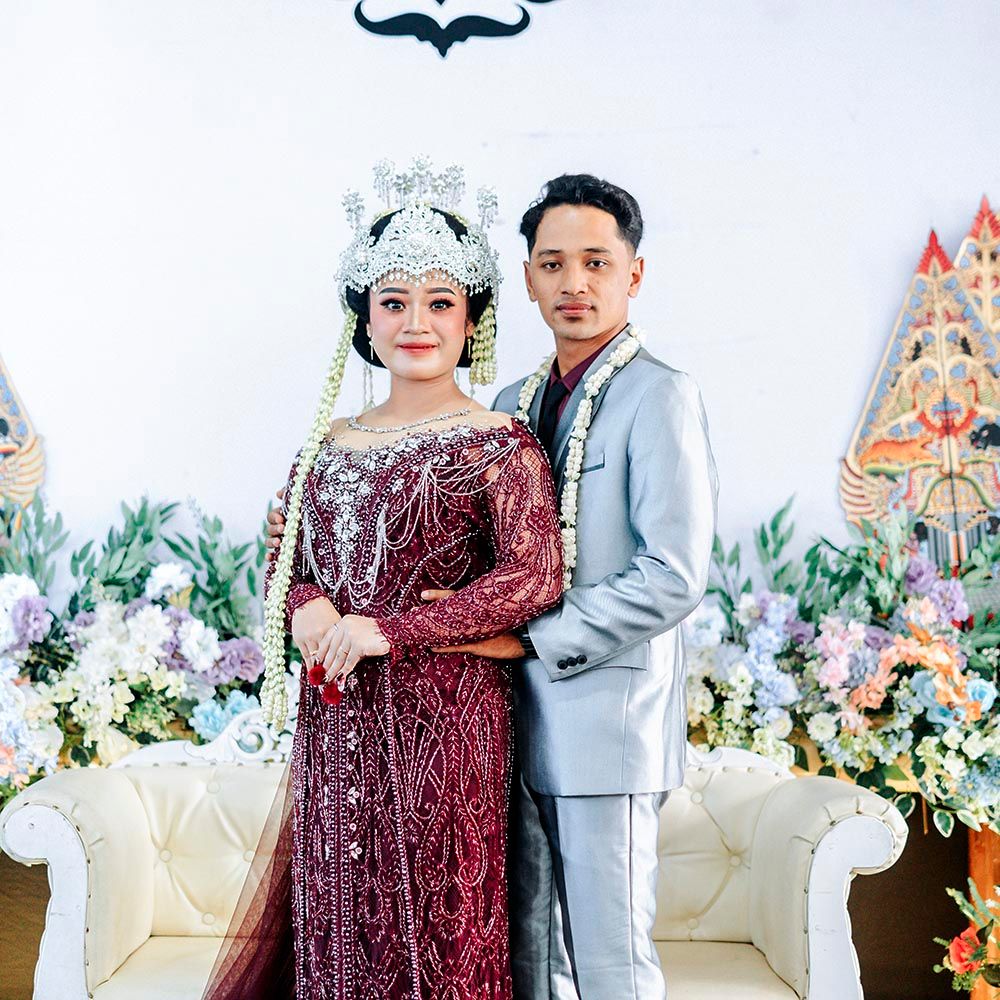 Bride and groom cutting elegant multi tiered white wedding cake decorated with fresh flowers at reception celebration