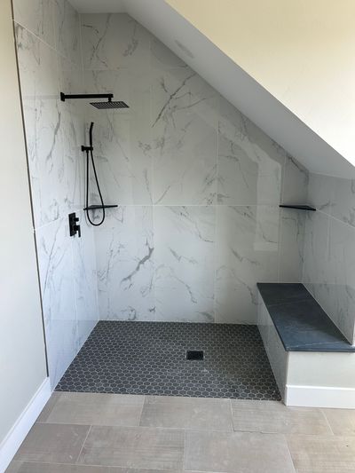 Custom shower under sloped ceiling with marble wall tile and built-in bench in Marble Falls, Texas