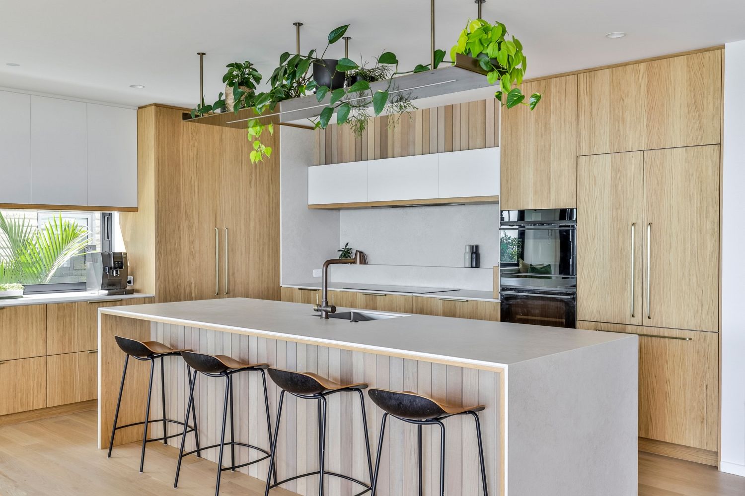 Modern oak kitchen with floating shelves and integrated appliances in a coastal home by Carlielle