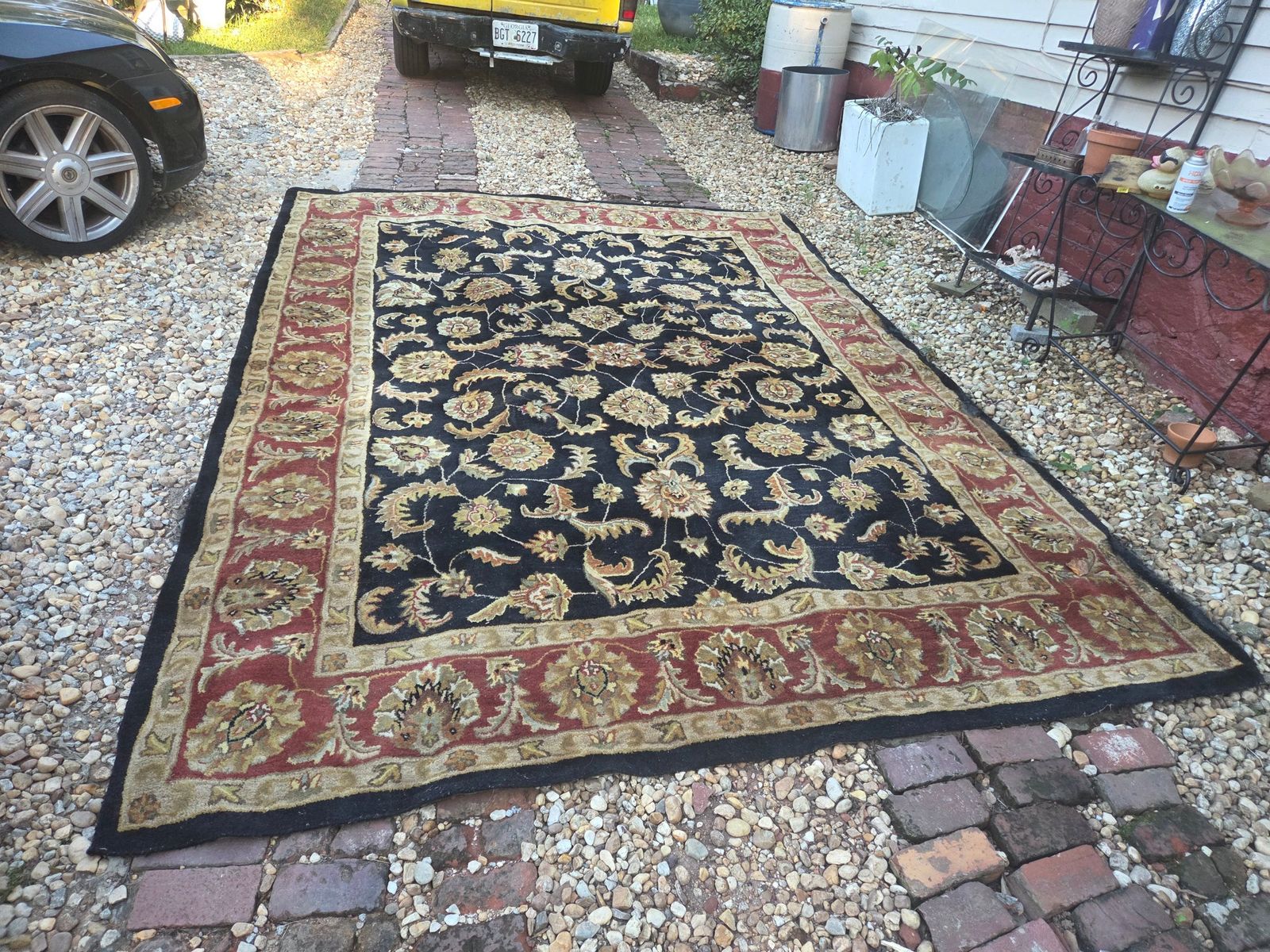 Large area rug with an ornate floral oriental-style pattern. The rug has a black center field with beige and gold floral motifs, surrounded by a wide red border with similar floral designs. The outer edge is finished in black. There is visible wear and fraying along one of the long edges. — photo 6