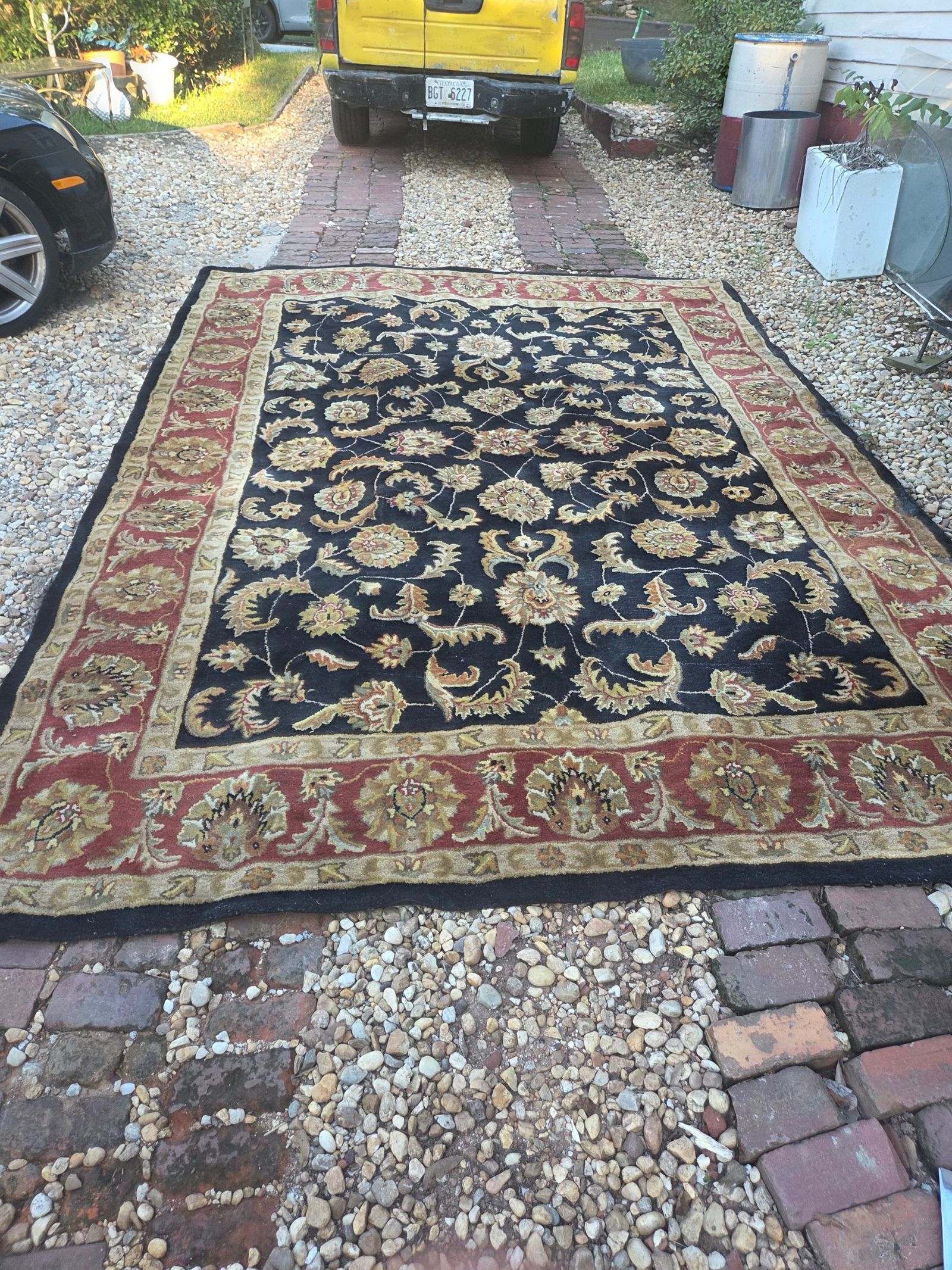 Large area rug with an ornate floral oriental-style pattern. The rug has a black center field with beige and gold floral motifs, surrounded by a wide red border with similar floral designs. The outer edge is finished in black. There is visible wear and fraying along one of the long edges. — photo 2