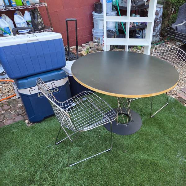 Table Mid-Century Modern Round Table $90.  2 Wire Chairs $45 ea 5 x 10 carpet 85. Mid-century modern dining a round table,  two wire side chairs. The table has a black laminate top with an exposed plywood edge and a black metal pedestal base with wire accents. The two chairs are constructed from chrome-plated steel wire with a sled base design.