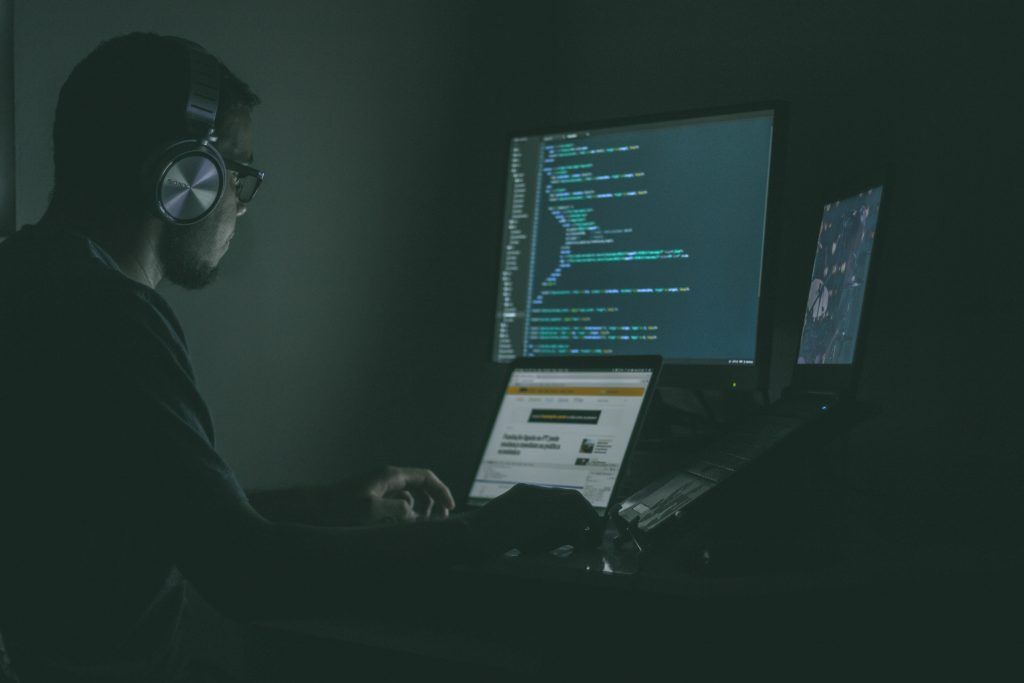 A programmer working at a laptop workstation in the dark