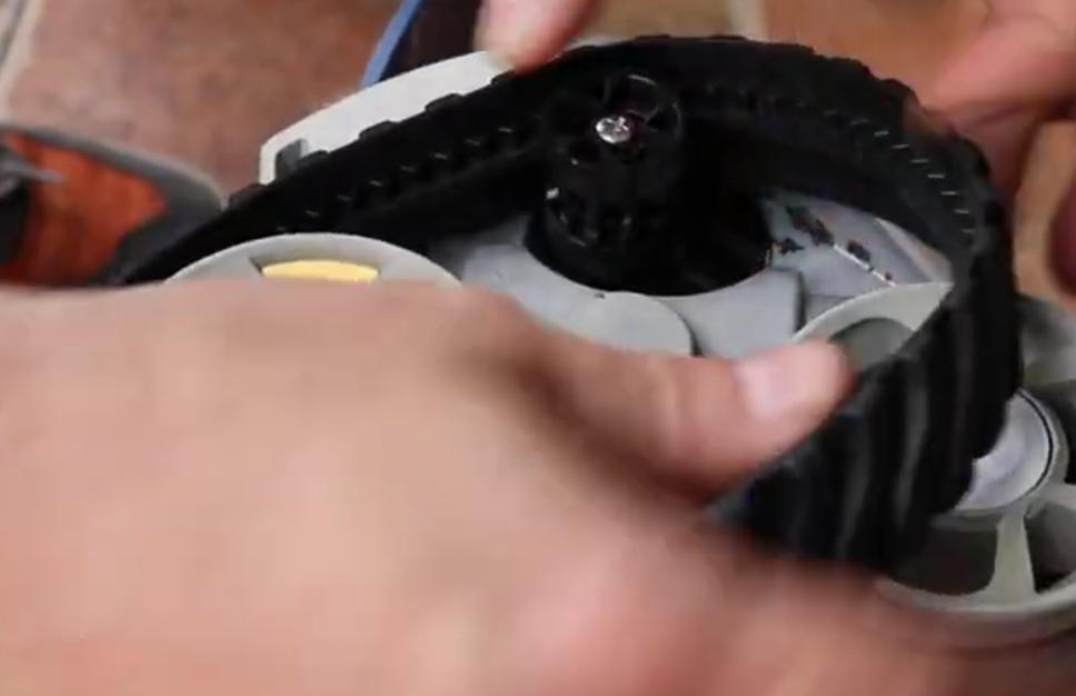Screenshot 2026-04-15 101802 Am - Diy Pool Resources - Inyopools.com Hands assemble a black toothed belt around a gray gear-driven mechanism in a close-up view.