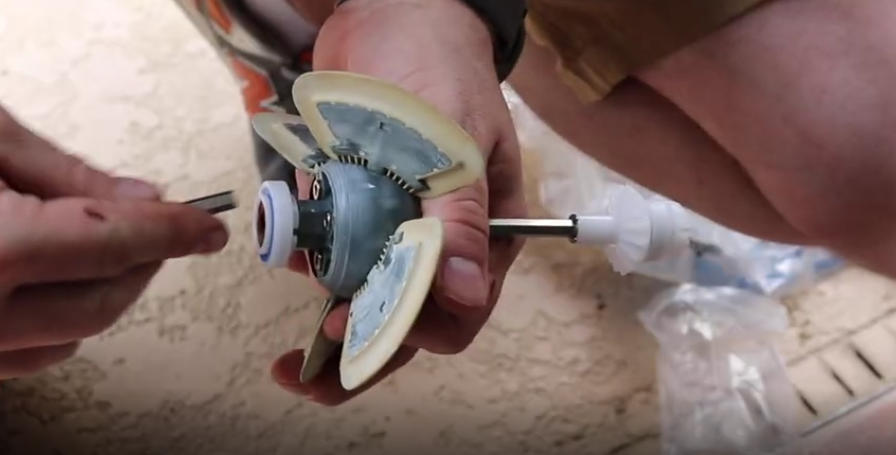 Screenshot 2026-04-15 101954 Am - Diy Pool Resources - Inyopools.com Close-up of hands assembling a small plastic impeller with white blades on a metal shaft, likely a pump or valve component.