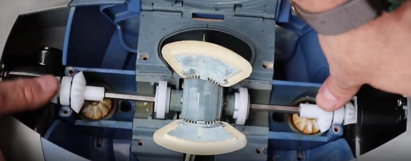 Screenshot 2026-04-15 104359 Am - Diy Pool Resources - Inyopools.com Close-up of a blue machine showing a central rotating shaft with two white gears on either side, hands holding the assembly apart for maintenance/repair.