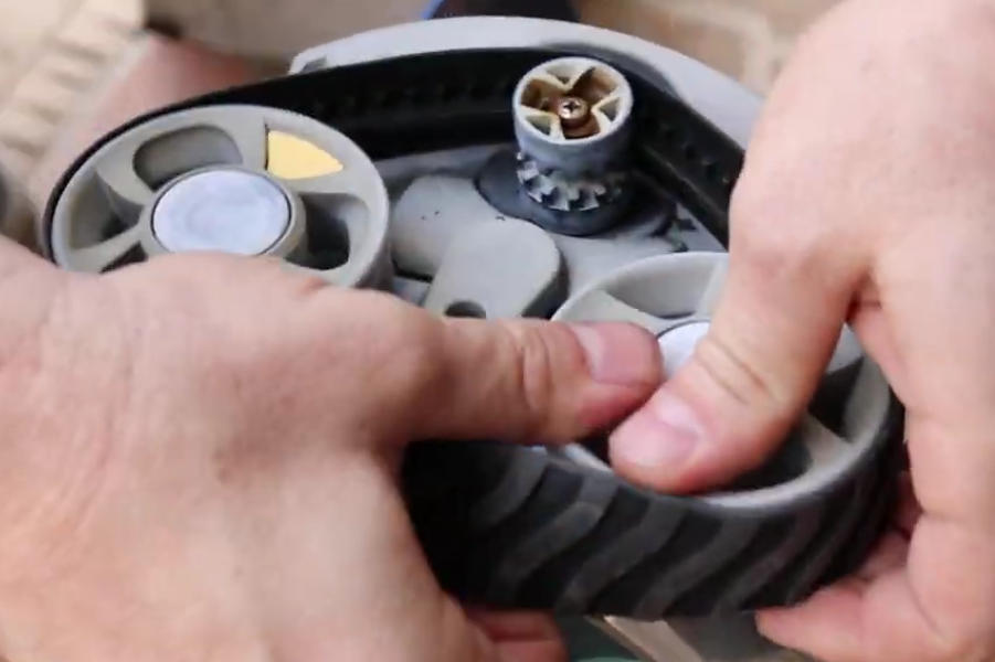 Screenshot 2026-04-15 95751 Am - Diy Pool Resources - Inyopools.com Close-up of hands fitting a gray, ribbed drive wheel onto a small mechanical assembly.