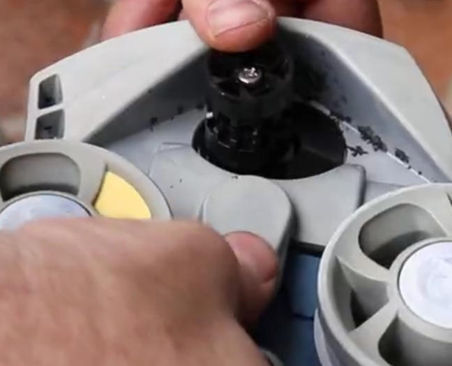 Screenshot 2026-04-23 94650 Am - Diy Pool Resources - Inyopools.com Close-up of hands assembling a gray plastic device with two circular rotating wheels and a central black connector.