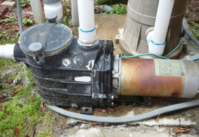 Outdoor pool pump and motor connected to white PVC pipes on a concrete pad.