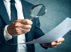 Tax inspector investigating financial documents through magnifying glass, forensic accounting or financial forensics, inspecting offshore company financial papers, documents and reports.