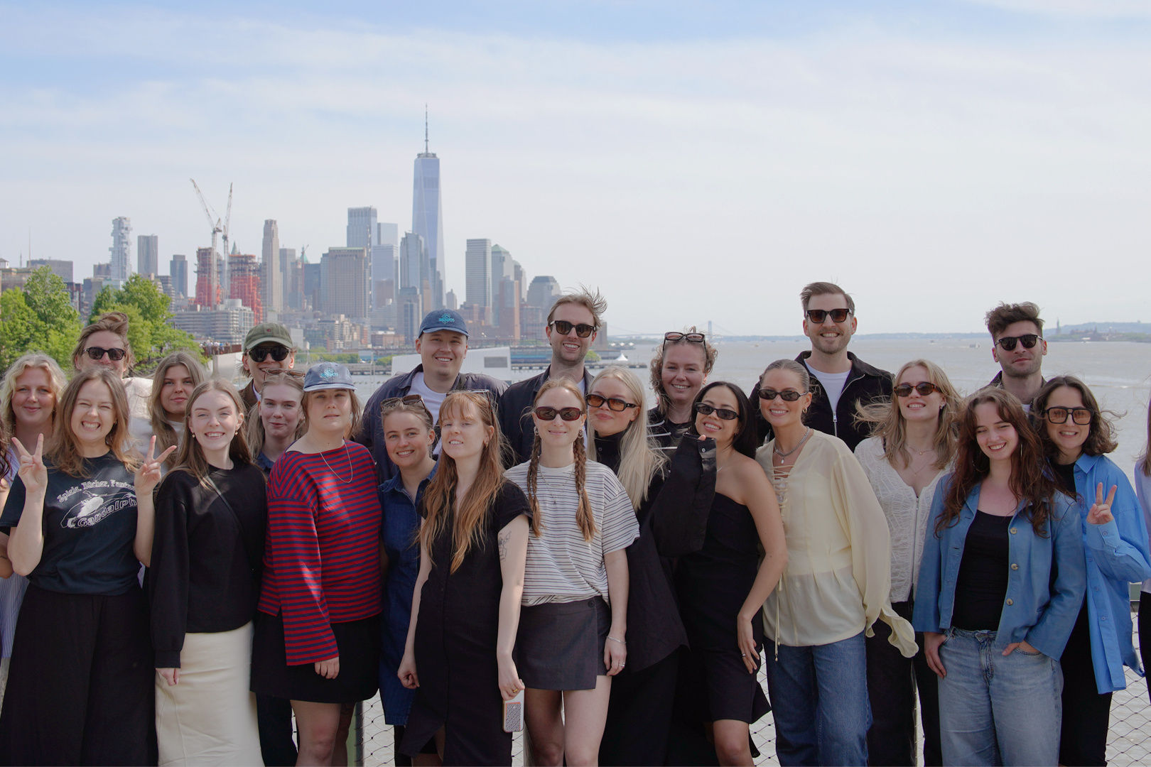 23 Berghs studenter ler in i kameran med New York siluett i bakgrunden en solig dag.
