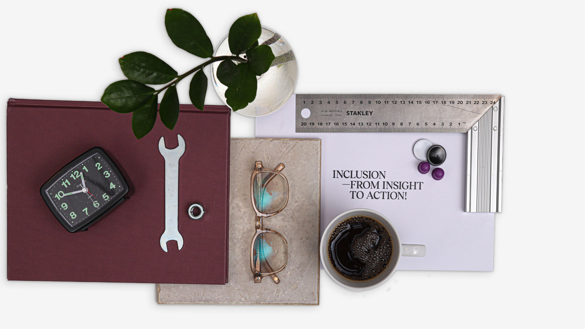 A composition with a notebook, a wrench, a pair of reading glasses, a plant and a cup of coffee. The picture represents tools and ideas related to studying at Berghs School of Communication