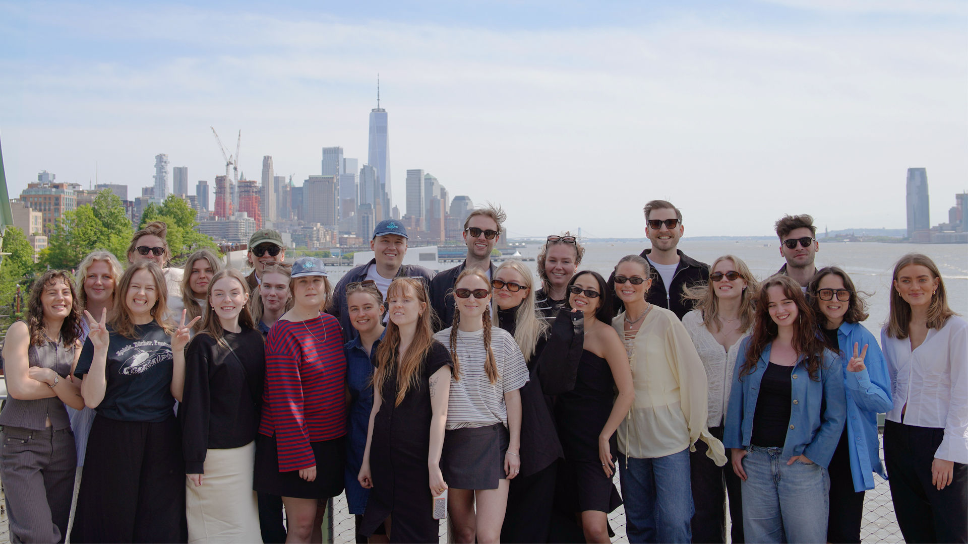 23 Berghs studenter ler in i kameran med New York siluett i bakgrunden en solig dag.