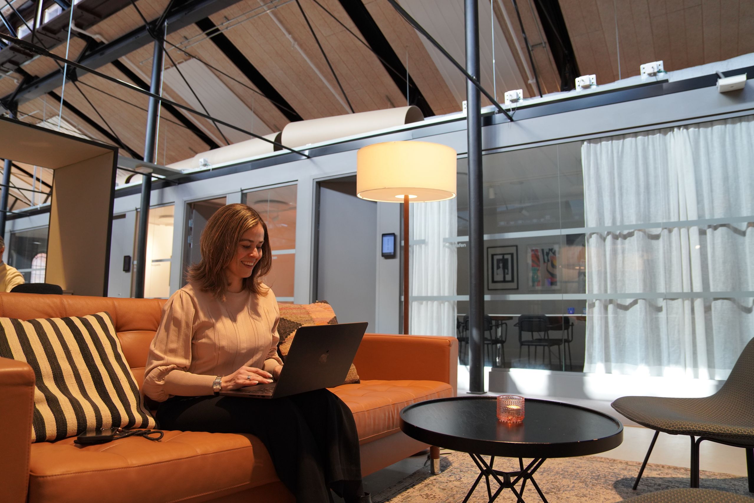 En kvinna sitter i en brun lädersoffa och arbetar på sin laptop.