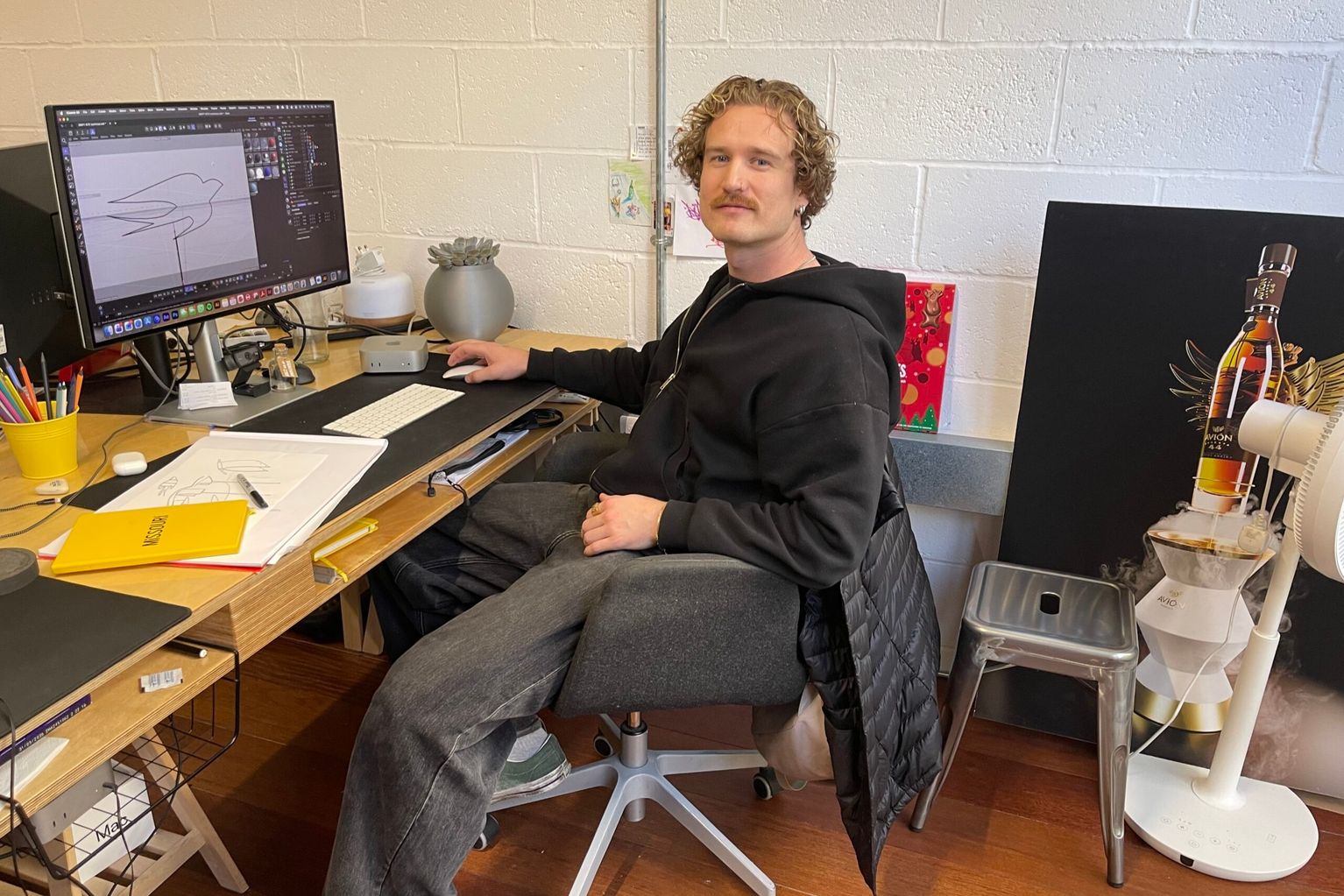 Axel Valberg sitting as his desk, on the computer screen a design of a bird graphic can be seen.