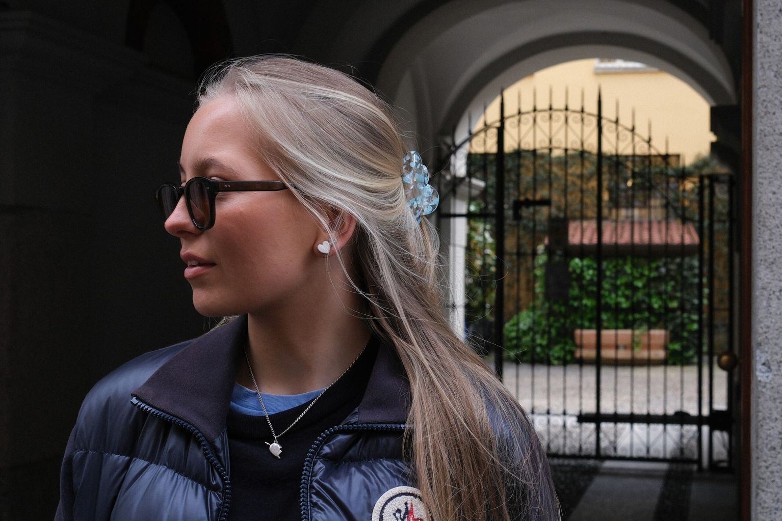 Clara Werner is looking away from the camera, in the background a Milanese cast iron gate can be seen.