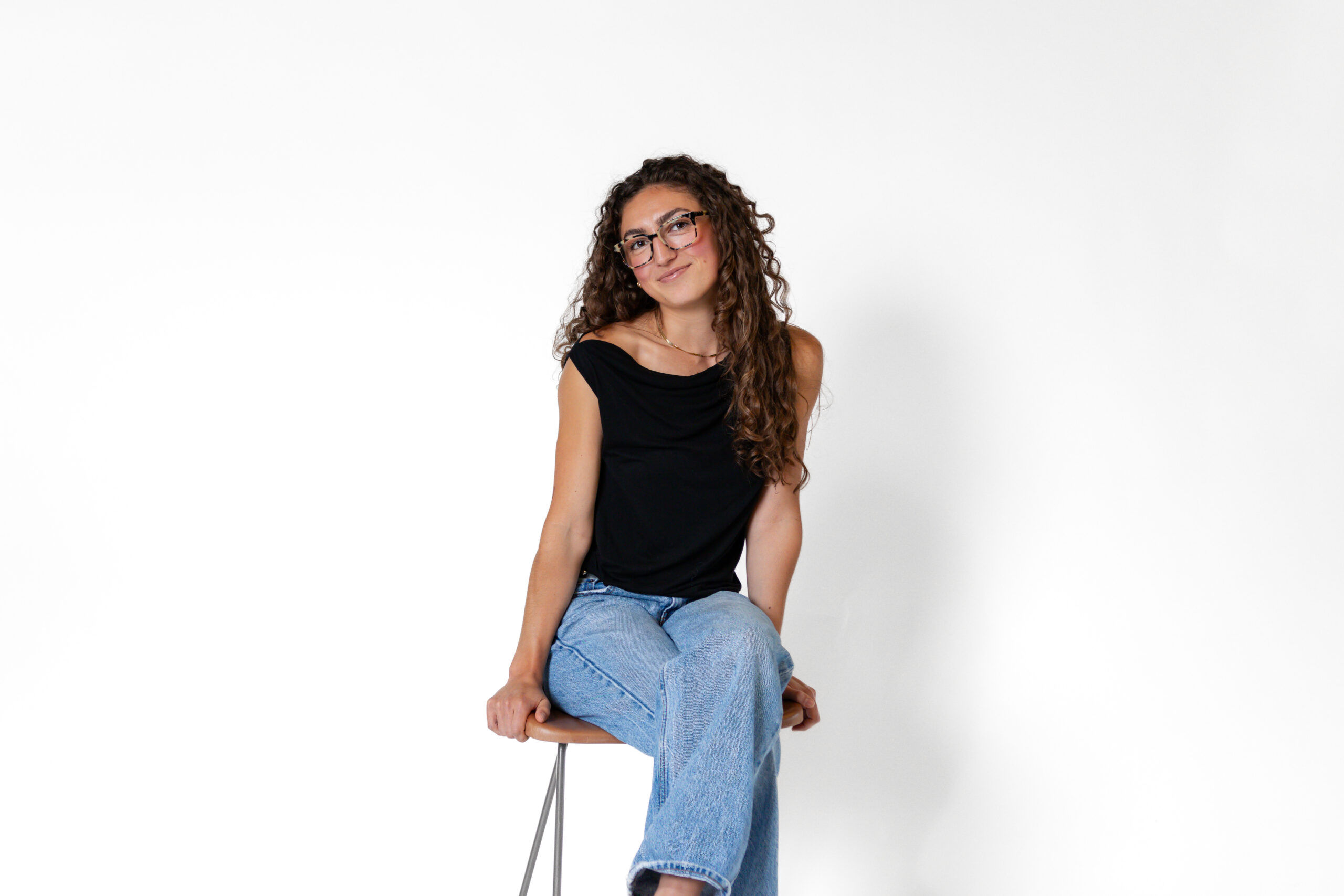 A photo of Emma Thomas sitting on a high stool, smiling at the camera.