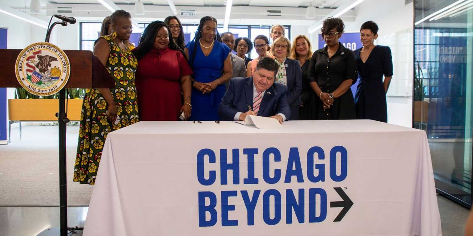 Governor JB Pritzker and Lieutenant Governor Julianna Stratton signing the birth equity legislation into law ontop of a table in Chicago Beyond