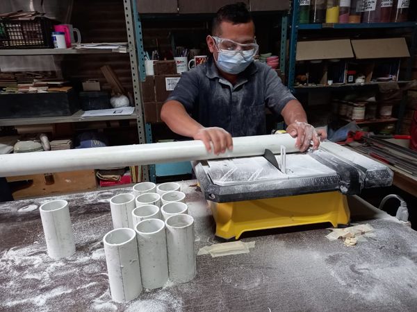 A photo of an artisan sawing PVC pipe to make a custom candle mold