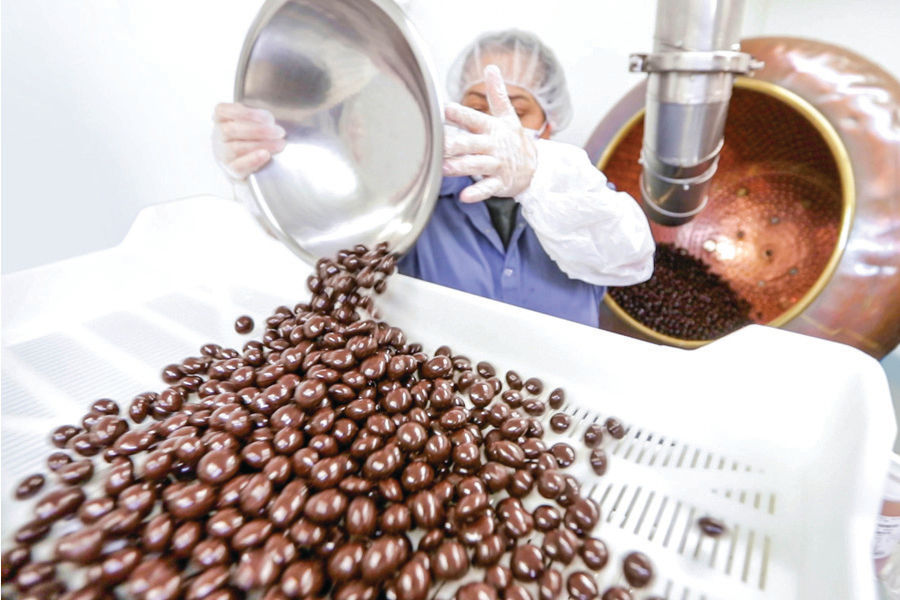 Chocolate covered cherries being poured from metal bowl into plastic tray