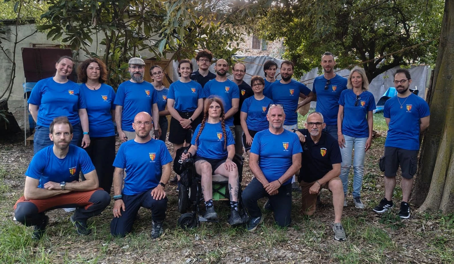 Un gruppo di sette individui in abiti medievali, in piedi davanti a una grande tenda bianca al tramonto, con in mano vari oggetti di scena e armi.