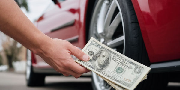 person fanning cash in front of car wheel