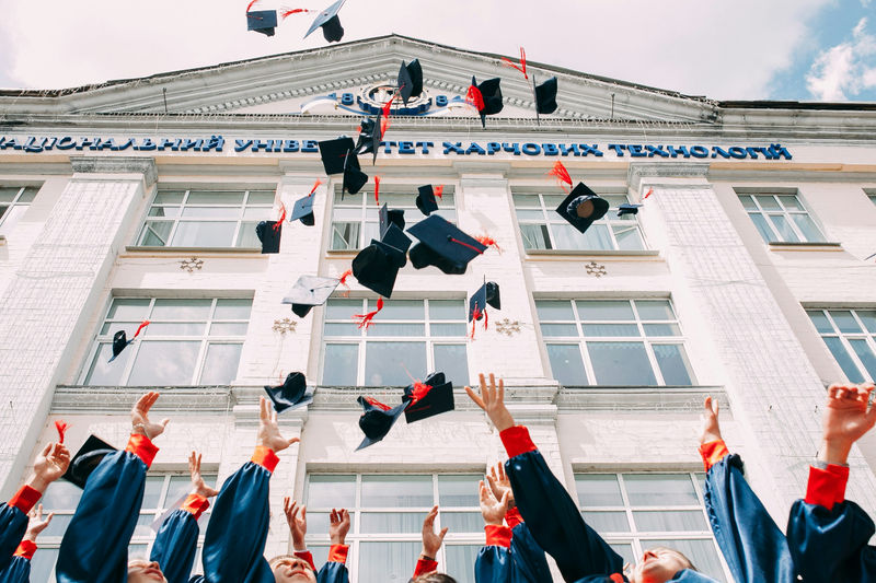 A group of students celebrating graduation by tossing caps into the air outside a university building.