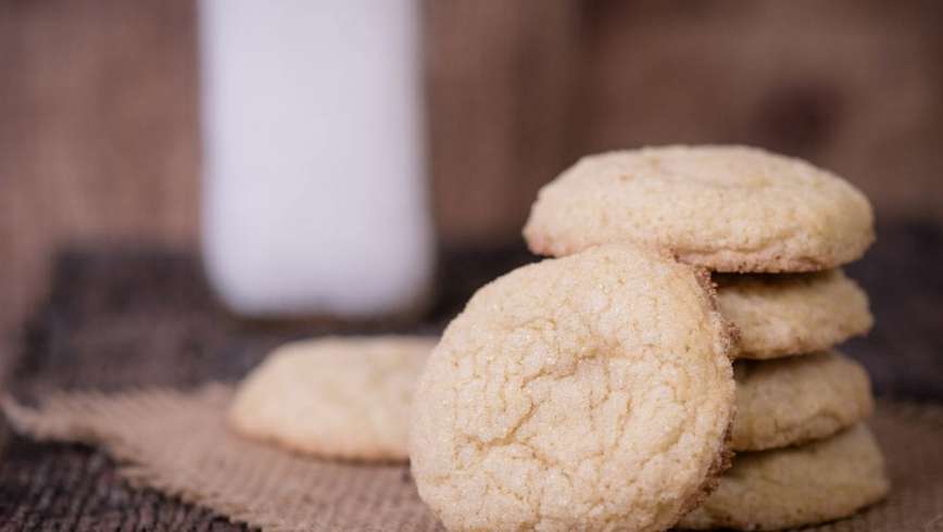 a stack of weed sugar cookies on a rustic wooden surface with more sugar cookies around the stack