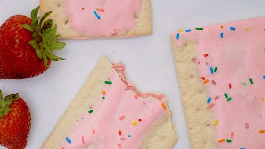 Lots of pink weed pop tarts spread out on the table with strawberries and sprinkles spread on the table to