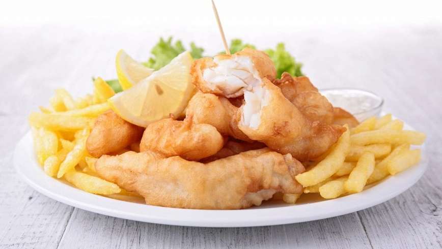 weed fish and chips on a white plate with lemon and salad in the background