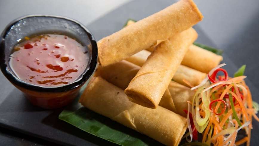 For cannabis infused spring rolls on a black plate with two Kabah spring rolls make it a TP on top of them. Sweet-and-sour sauce and veggies beside the spring rolls on the plate