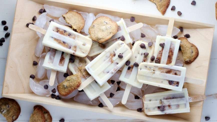 Oreo infused Popsicles with cookies and chocolate chips spread around them the Popsicles are on ice cubes in a wooden box