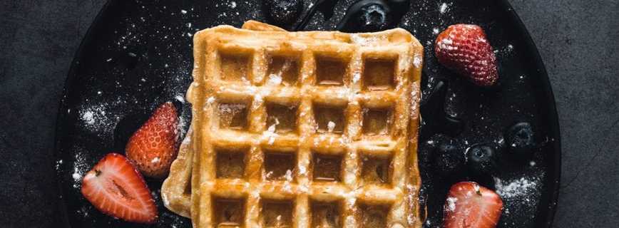 cannabis infused waffle on a black plate with maple syrup poured overtop of them. Strawberries and icing sugar spread around on the black plate.