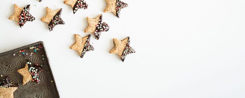 star shaped cookies, half covered in chocolate and sprinkles. alligned artistically with some on baking tray and some on a white table