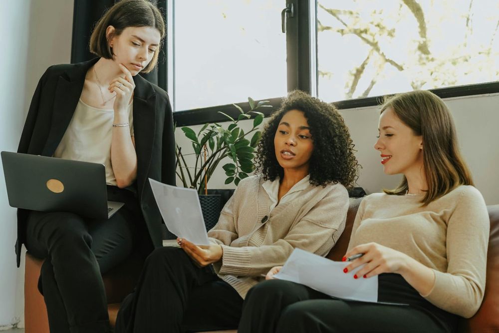 Three colleagues reviewing a printed resume together on a couch