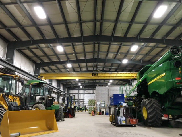 High-bay LED lighting over an agricultural equipment service shop with a combine, tractor and loader