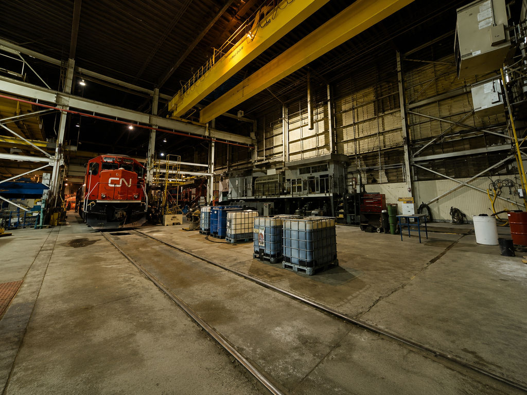 Red locomotive inside a rail maintenance shop under dim overhead lighting