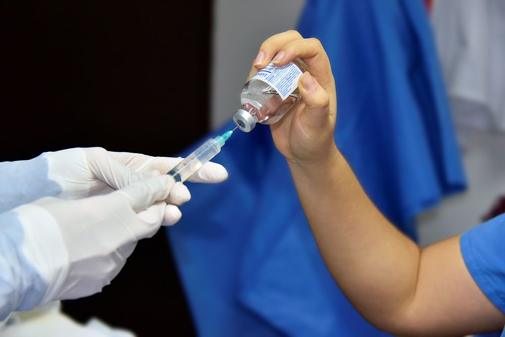 A syringe needle puncturing the grey rubber septum of a vial through its metal crimp cap