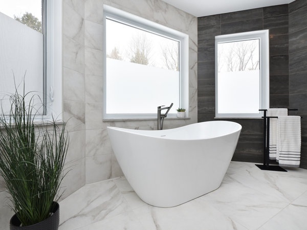 Luxury modern bathroom with a sculptural white soaking tub, set against contrasting light marble and dark slate accent tiles.