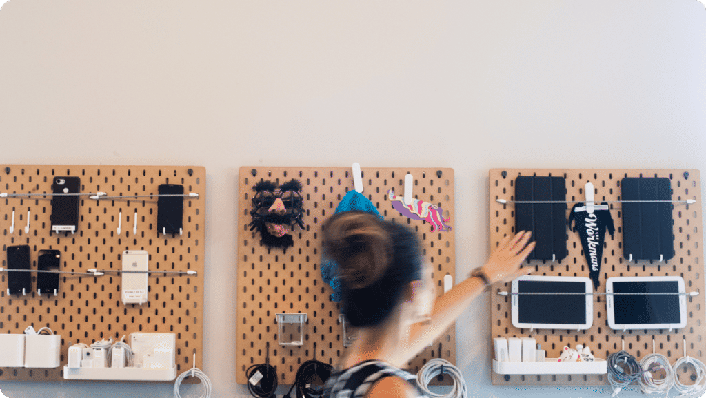 A quick moment captured in Cuttlesoft's mobile testing lab shows a team member reaching for one of many devices mounted on our testing wall. The organized pegboard system displays various smartphones and tablets - essential tools for ensuring our mobile applications work seamlessly across different devices. Charging cables and testing accessories are neatly arranged, making it easy for developers to grab what they need. This setup helps us test apps in real-world conditions before they reach users' hands. The motion blur in the image adds energy to the scene, showing how our team actively works with these tools throughout the development process.