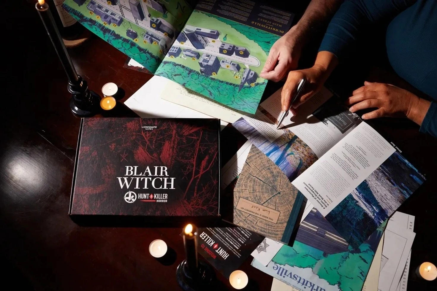 A compelling visual display highlighting Cuttlesoft's custom software solution for Hunt A Killer’s Blair Witch themed box. The image features an intricately arranged tableau on a dark wooden table, illuminated by soft candlelight. A central Blair Witch Hunt A Killer box lays prominently, surrounded by various game components including detailed maps, intriguing narrative booklets, and engaging, cryptic clues designed to enhance the user experience of the murder mystery subscription box. Visible hands of two engaged participants are strategically placing and pointing at clues, demonstrating the interactive and investigative nature of the game. This scene perfectly embodies the seamless integration and functionality of the custom web application developed by Cuttlesoft, utilizing technologies such as Rails, React, and Sidekiq housed on the Heroku platform. The application supports a dynamic, multi-brand shopping cart, sophisticated logistics management for tax and shipping calculations, and robust administration tools for enhanced operational efficiency in the e-commerce sector. The image not only showcases the product's appeal but also symbolizes Cuttlesoft's expertise in creating comprehensive, scalable software solutions that cater specifically to customized client needs in the entertainment and e-commerce industries.
