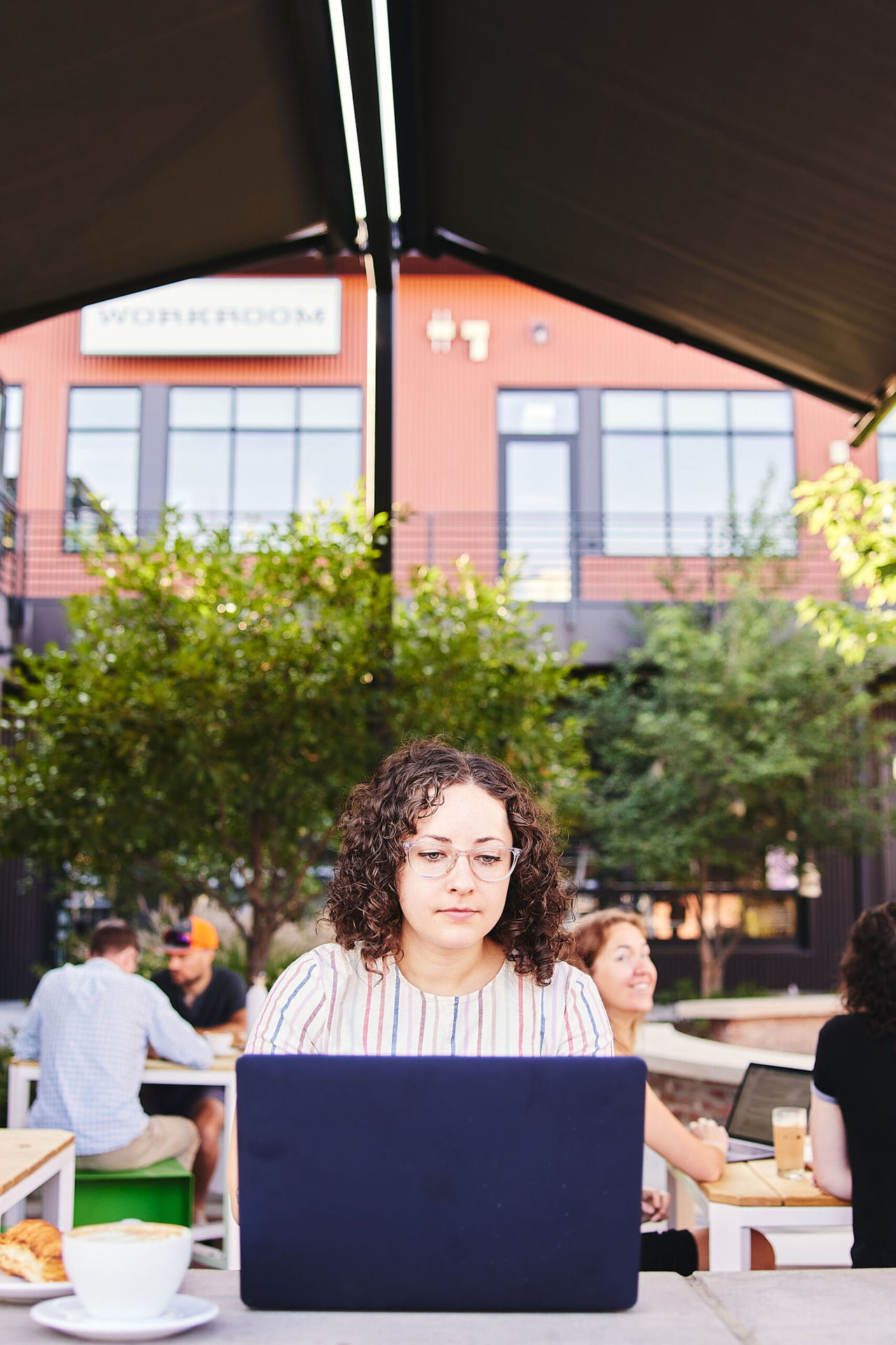 Marisa works on a JavaScript project from a coffee shop while Sara looks on with a smile.
