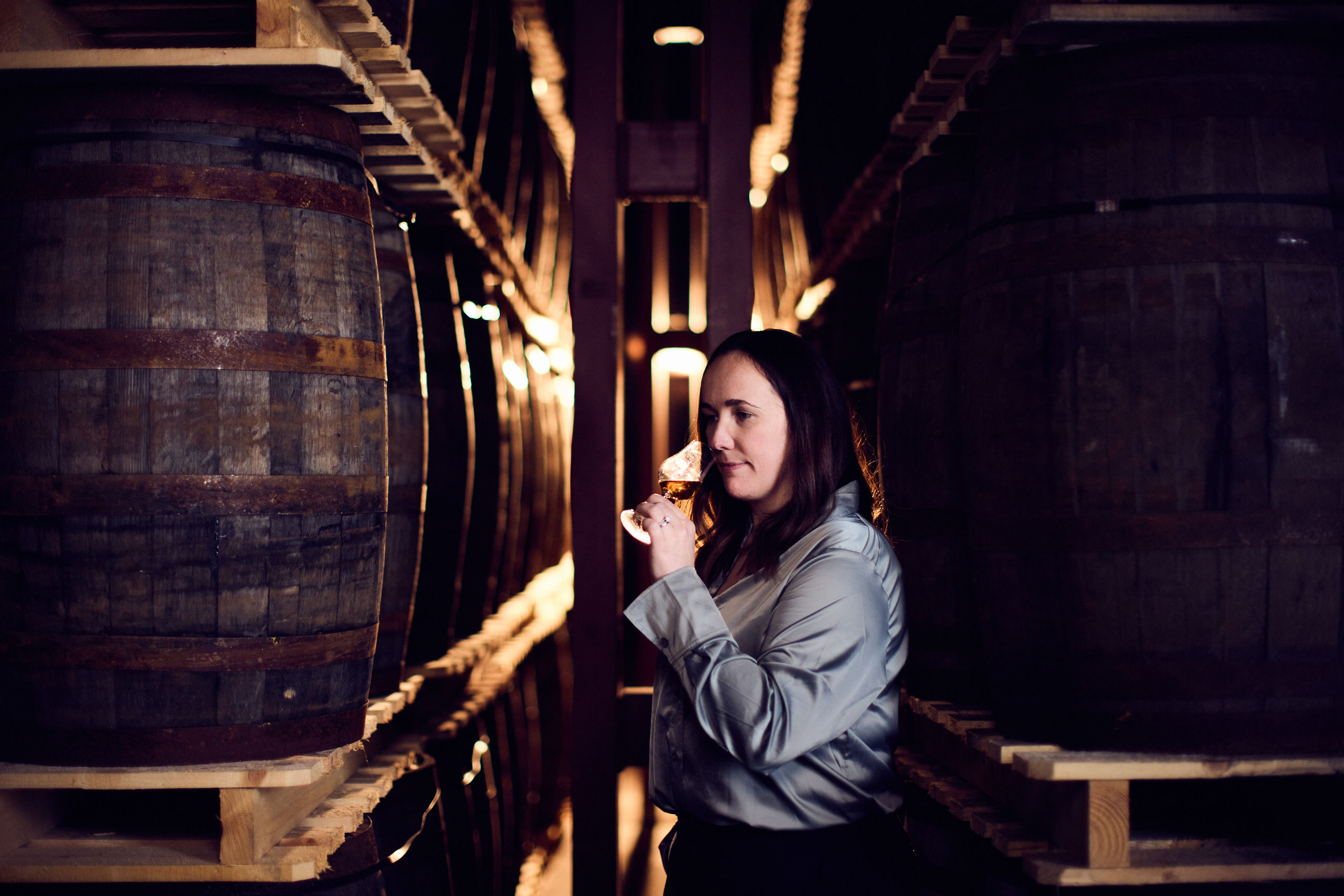 A person smelling Dalmunach whisky from a tasting glass inside a distillery