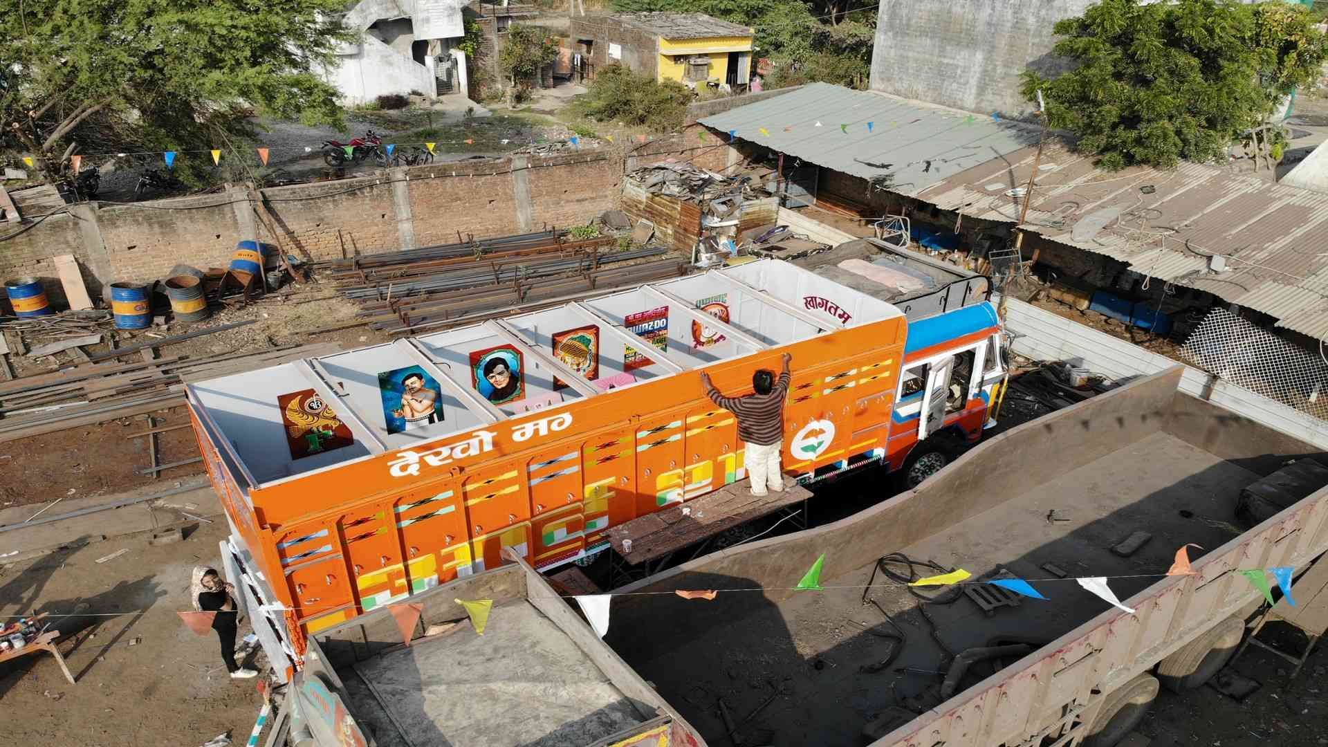 Artist painting traditional Indian truck art on an orange cargo truck