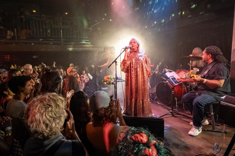Asha Puthli performing live on stage in a golden outfit with her band