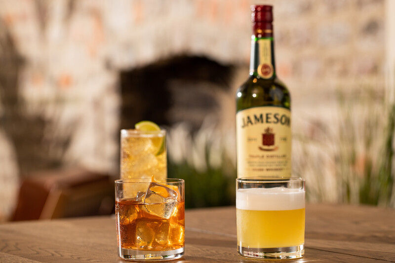 Three whiskey cocktails on a table with a bottle of Jameson Irish Whiskey behind them