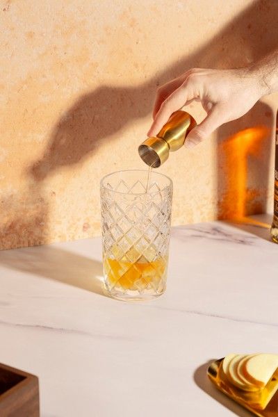 Hand adding bitters to a mixing glass with citrus and ice while preparing an old fashioned cocktail
